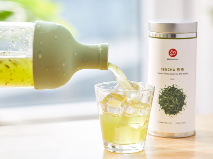 pouring sencha green tea in a glass full of ice place beside sencha tea tin