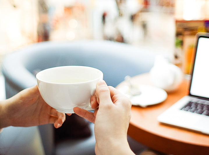 hand holding a white cup with laptop in front