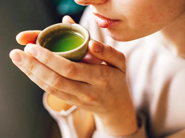 Close-up of a person mindfully sipping vibrant green tea from a small ceramic cup, conveying calm focus and the stress-relieving ritual of Japanese tea drinking