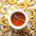 Roasted delicata squash on baking sheet with cup on marinara in center for dipping.