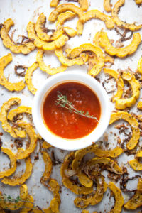 Roasted delicata squash on baking sheet with cup on marinara in center for dipping.