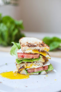 Fried egg blt cut in half and stacked on top of each other on a plate.