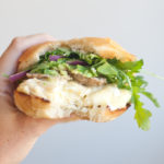Hand holding egg sandwich with bite taken out of it.