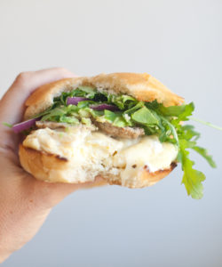 Hand holding egg sandwich with bite taken out of it.