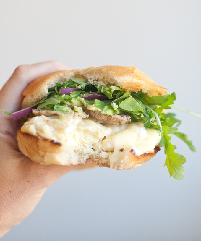 Hand holding egg sandwich with bite taken out of it.