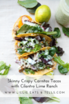 Three crispy carnitas tacos topped with fresh greens, sliced radishes, cheese, and creamy cilantro lime ranch are artfully arranged on a white surface with a zesty lime and leafy greens nearby. Text: Skinny Crispy Carnitas Tacos with Cilantro Lime Ranch.