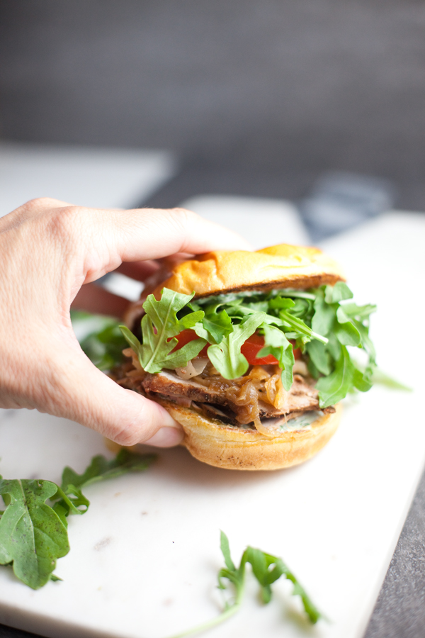 A hand grabbing a Pork Tenderloin Sandwich with lots of arugula stuffed inside