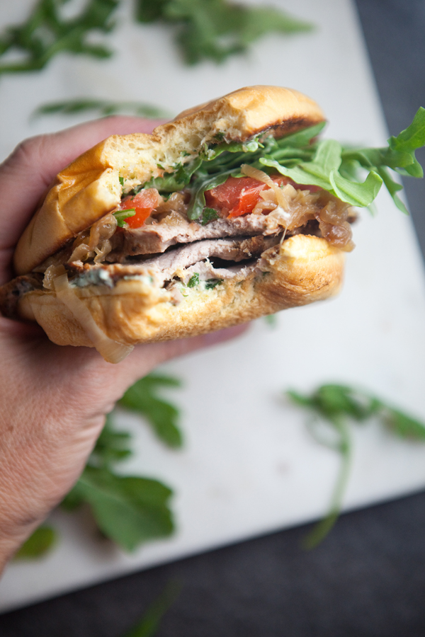 Pork Tenderloin Sandwich with lots of arugula being held with a bite taken out of it.