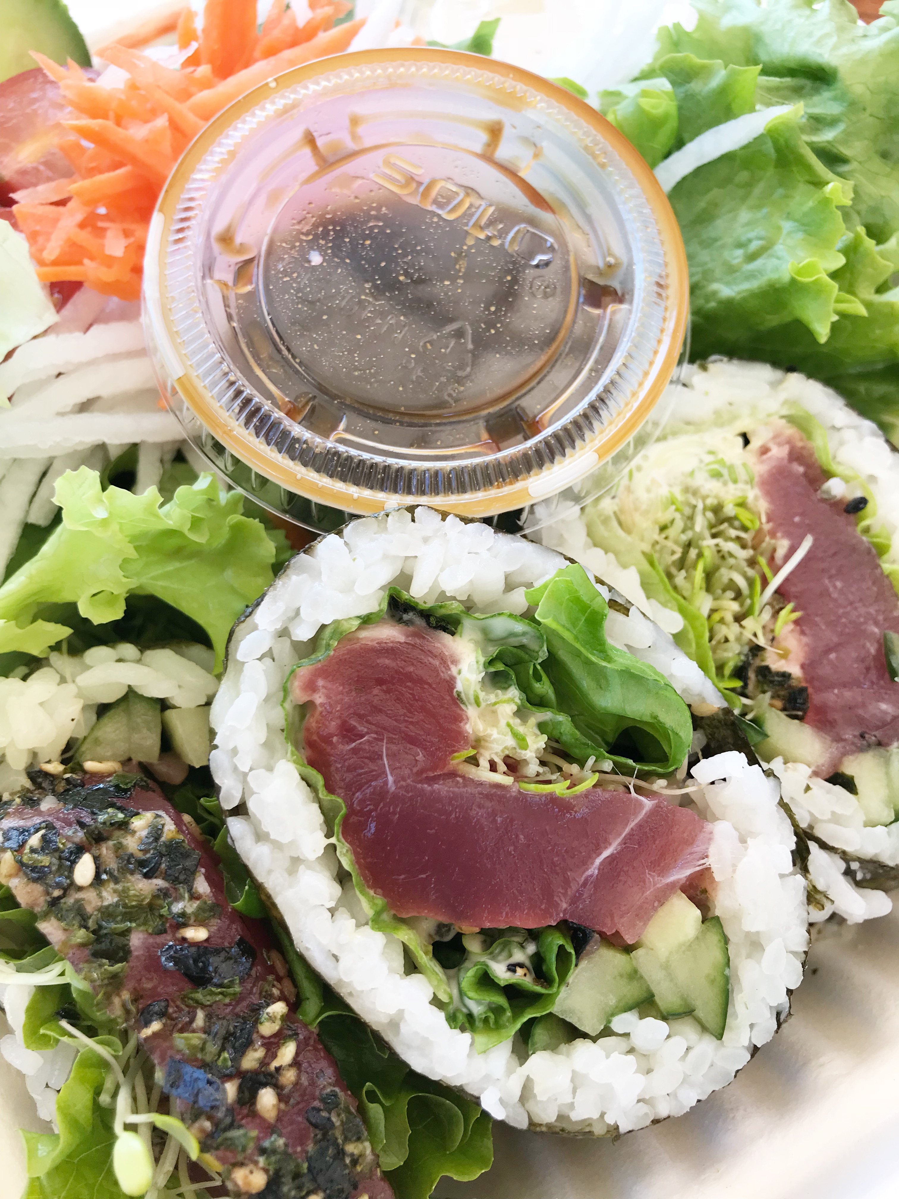 Close-up of sushi rolls filled with raw tuna, lettuce, cucumber, and sprouts—perfect for those mindful of macro counting—served with a side of soy sauce, shredded carrots, onions, and mixed greens.