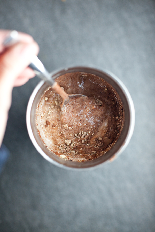 Chocolate protein shake in a large metal tumbler with metal spoon stirring in the powdered pbfit.