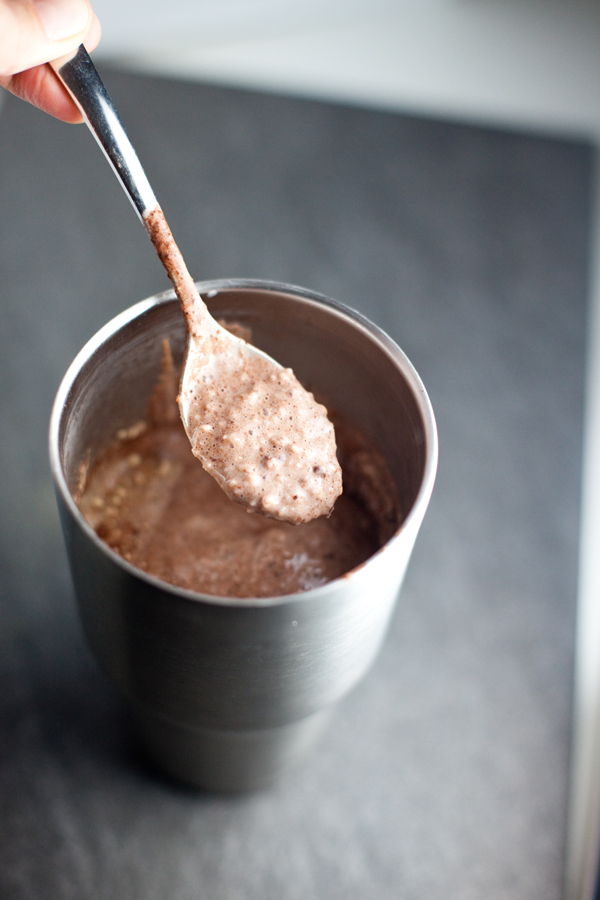 Chocolate protein shake in a large metal tumbler with spoon scooping out some of the shake.