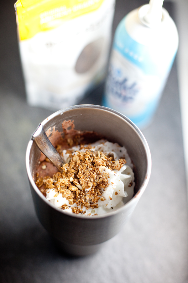 Chocolate shake in a large metal tumbler with whipped cream and granola on top and metal spoon in tumbler.