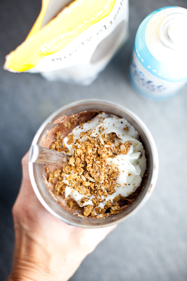 Protein shake in a large metal tumbler with whipped cream and granola on top and spoon.