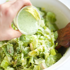 Pouring creamy jalapaño avocado dressing on a Mexican caesar salad