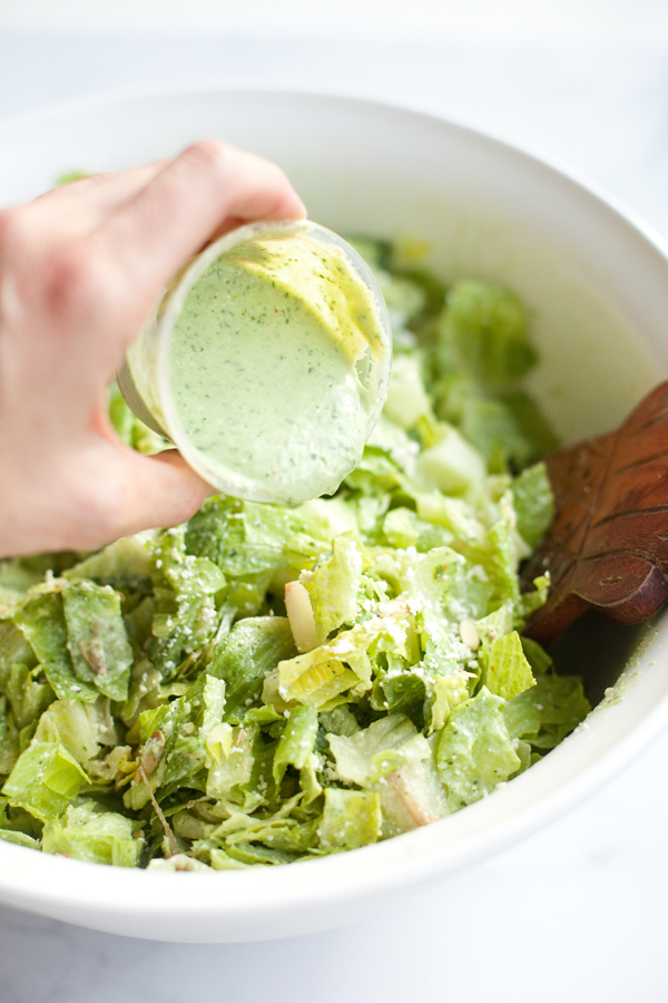 Pouring creamy jalapaño avocado dressing on a Mexican caesar salad