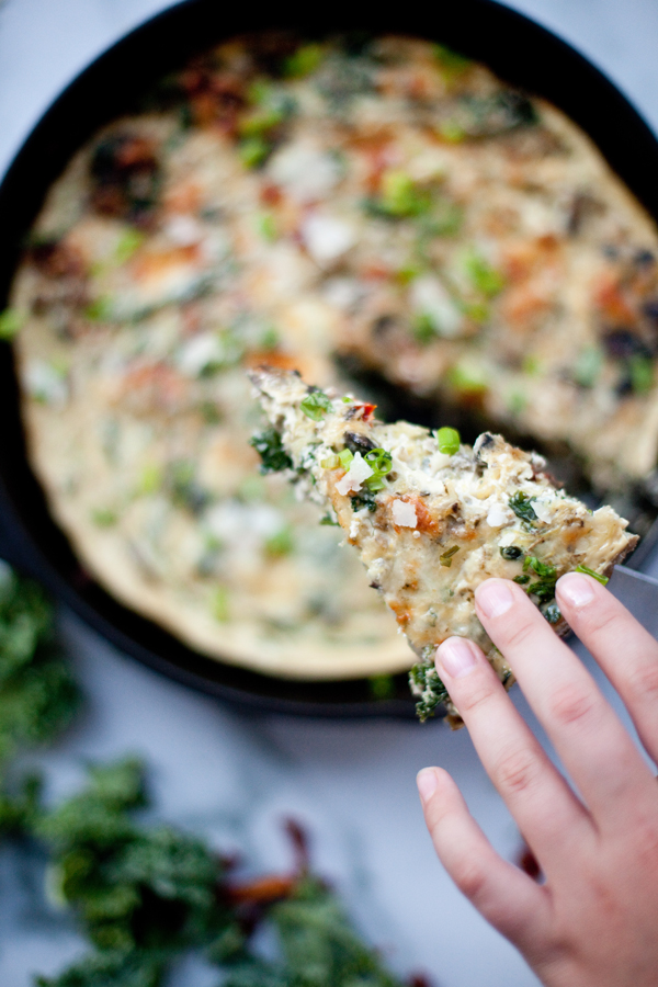 Hand lifting out a slice of turkey mushroom quiche out of cast-iron pan.