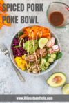 Enjoy an Easy Spiced Pork Poke Bowl: a vibrant medley featuring spiced pork, sliced avocado, radish, cucumber, carrots, red cabbage, mango, and rice. This colorful bowl is drizzled with savory sauce and served with a fork, extra sauce cup, half avocado, and website link—all beautifully arranged on a gray surface.