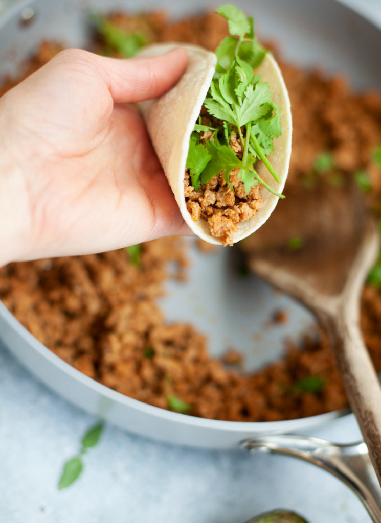 Ground turkey taco meat wrapped into tortilla to make taco and garnished with cilantro.