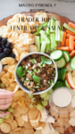 A platter featuring Trader Joe’s Lentil Dip in a bowl, surrounded by crackers, chips, sliced cucumber, carrots, celery, blackberries, and salad dressing. Text on the image describes this as a macro-friendly recipe.