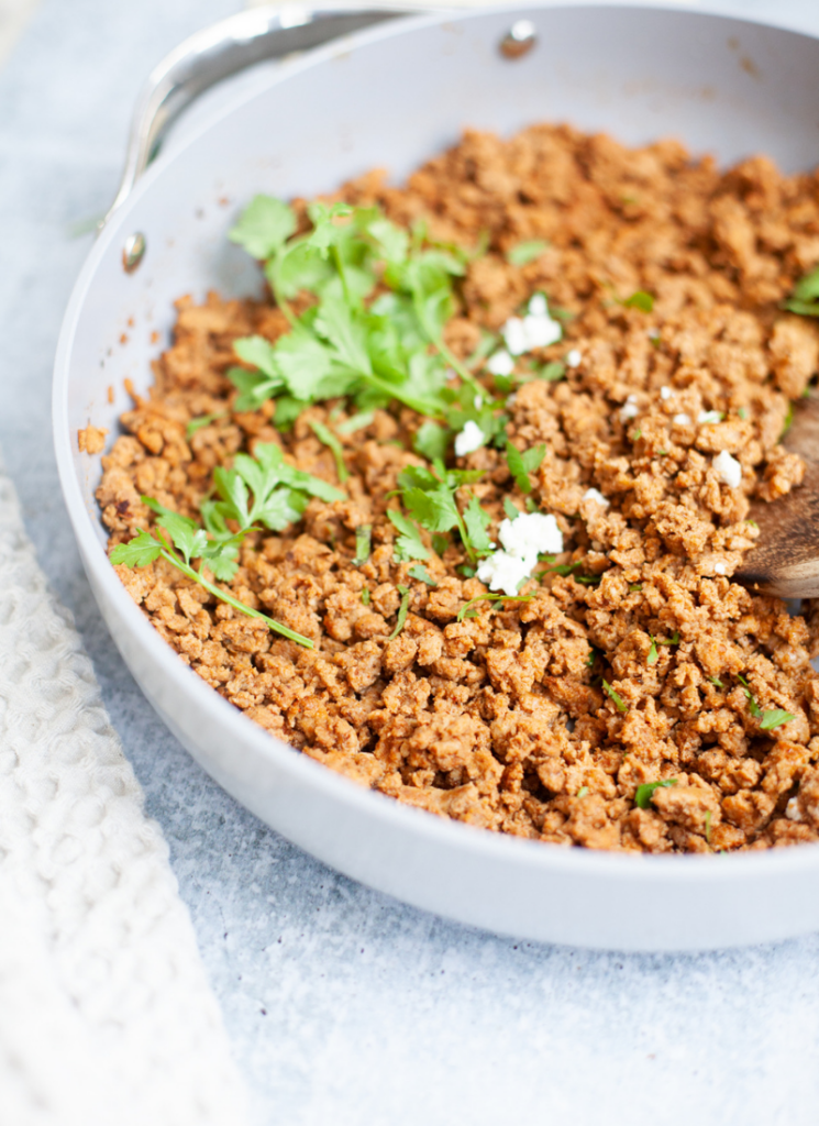 Ground turkey taco meat in skillet garnished with cilantro and a little bit of cotija cheese.