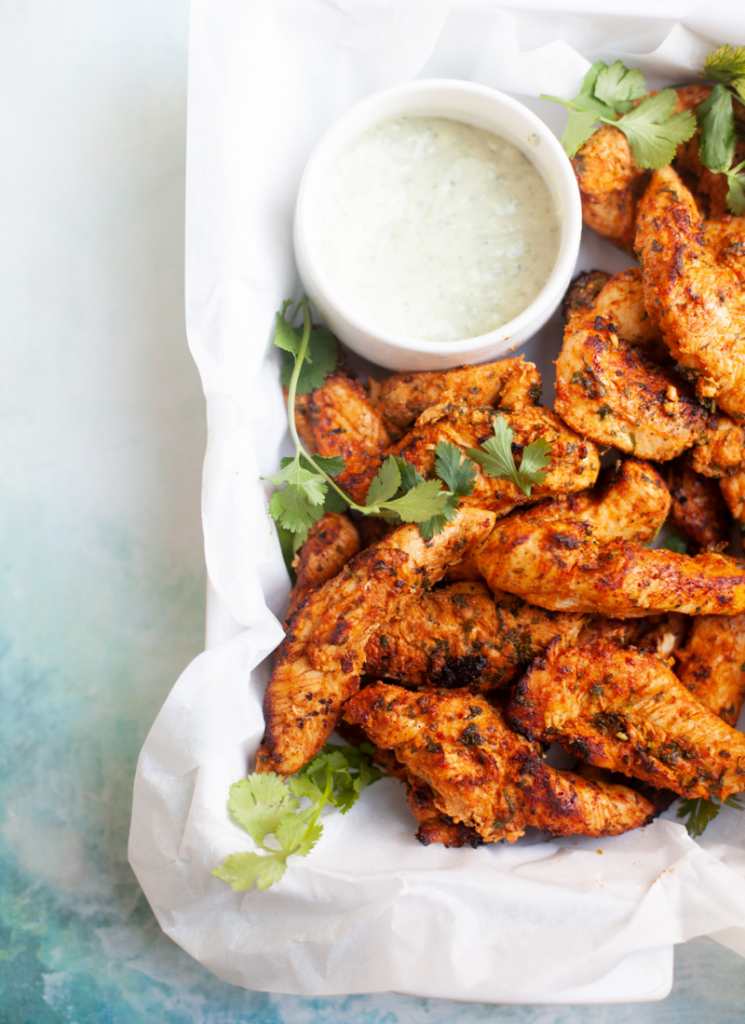 Air fryer chicken tenderloins garnished with cilantro in a parchment-lined serving platter.