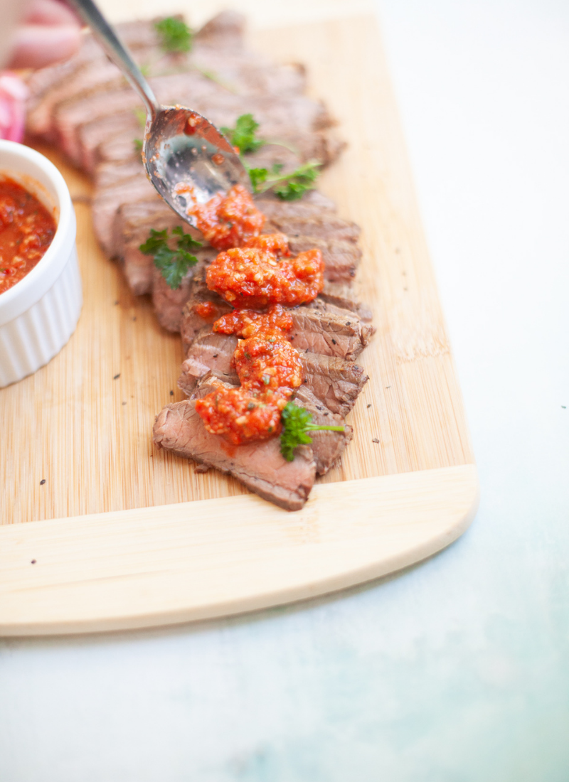 Romesco Sauce Drizzled on Top of Steak on a wooden cutting board.
