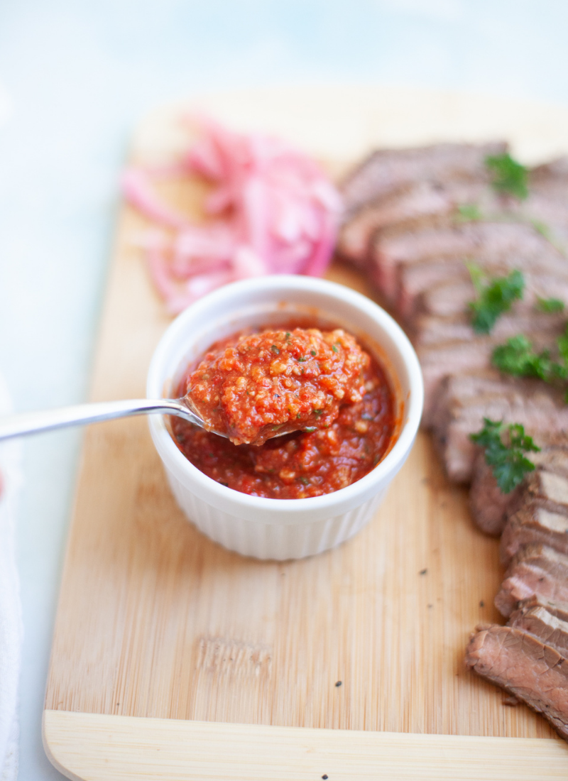 Metal Spoon scooping up small amounts of Romesco Sauce on a wooden cutting board.