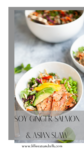 A white bowl filled with soy ginger salmon and Asian slaw, accompanied by sliced avocado and edamame, sits on a light surface. A smaller bowl and fresh herbs are in the background. Text reads Soy Ginger Salmon & Asian Slaw.
