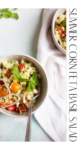 A bowl of corn feta and basil salad featuring sweet summer corn, juicy tomatoes, tangy feta, and fresh basil leaves, with red onion for extra flavor. A spoon rests in the bowl beside a crisp white napkin. Text reads SUMMER CORN FETA BASIL SALAD.