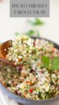 A wooden spoon scoops colorful tabouli salad with feta, brown rice, and cauliflower from a bowl, filled with chopped parsley, tomato, onion, and grains. Text above reads Macro Friendly Tabouli Salad.