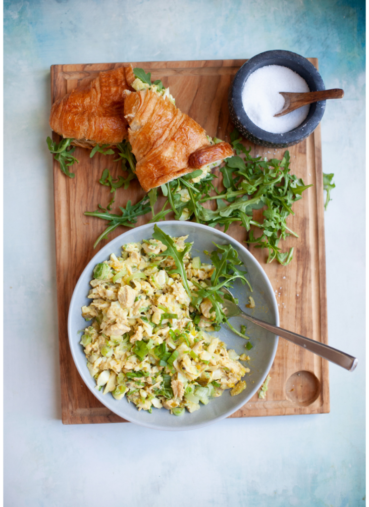 Pickle chicken salad on plate with fork on top of wood cutting board with croissant and arugula on the side.