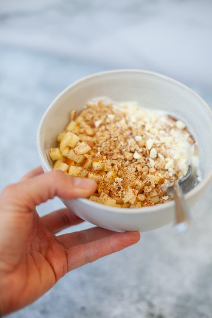 Hand holding apple crisp cottage cheese yogurt bowl with spoon.
