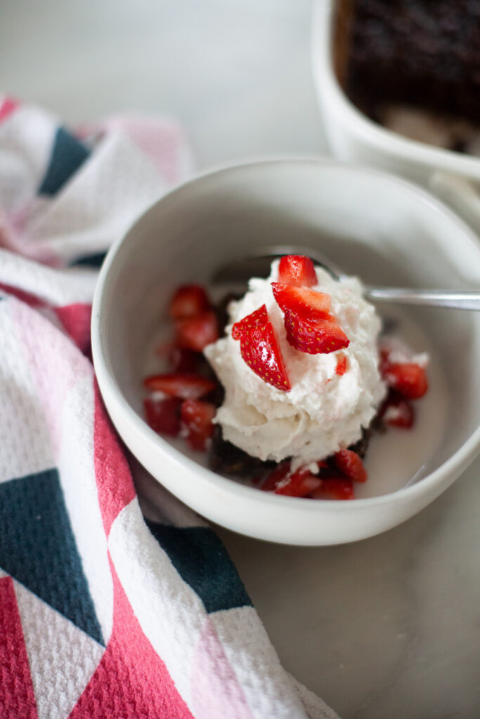 Brownie batter squash oats in white bowl with whipped cream and diced strawberries.