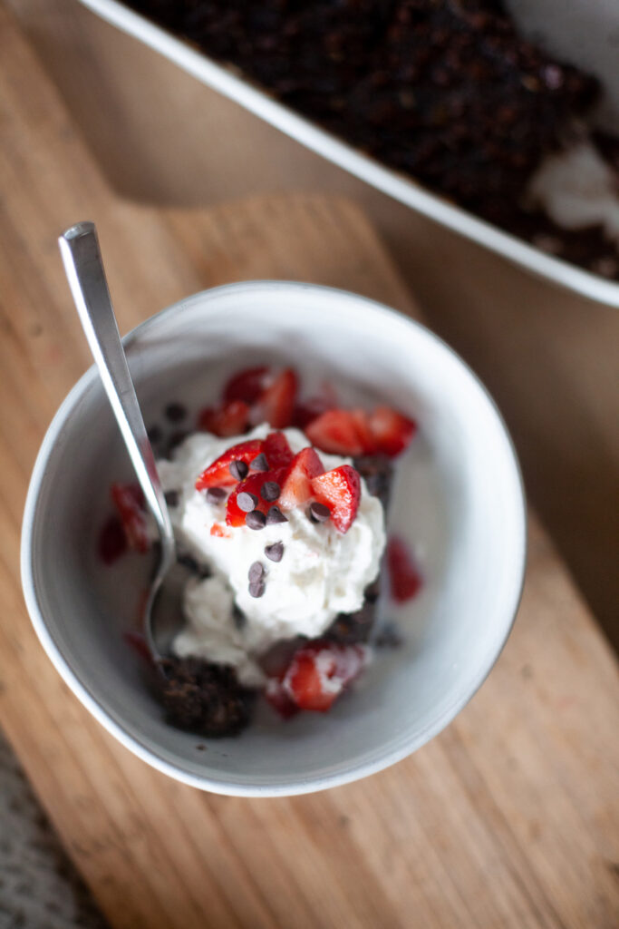 Brownie batter squash oats in bowl topped with whipped cream and strawberries.