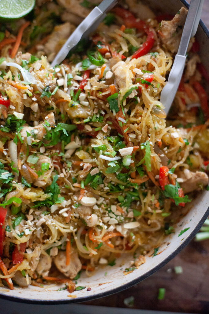 Spaghetti squash pad thai in skillet with serving tongs.