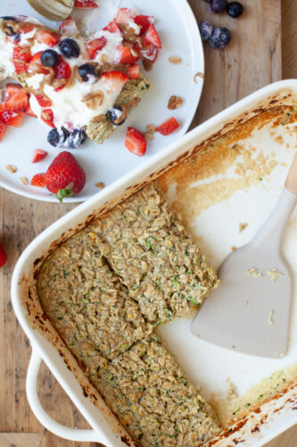 Baking dish of zucchini baked oats beside plate with slice of oats with toppings.