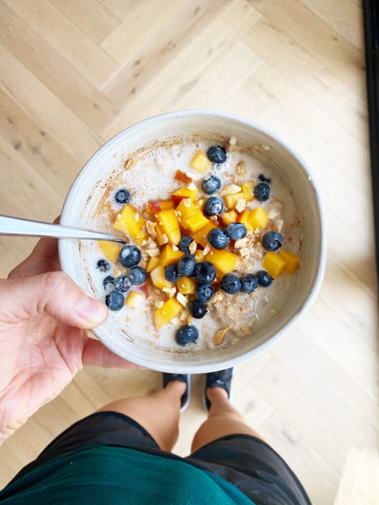 Hand holding a bowl of breakfast protein cauliflower oats with toppings.