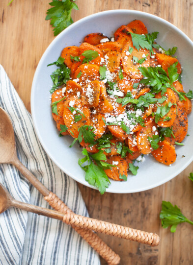Maple Cumin Roasted Carrots on a white plate topped with fresh parsley and goat cheese.