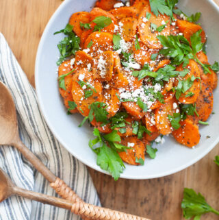 Maple Cumin Roasted Carrots on a white plate topped with fresh parsley and goat cheese.