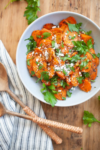 Maple Cumin Roasted Carrots on a white plate topped with fresh parsley and goat cheese.