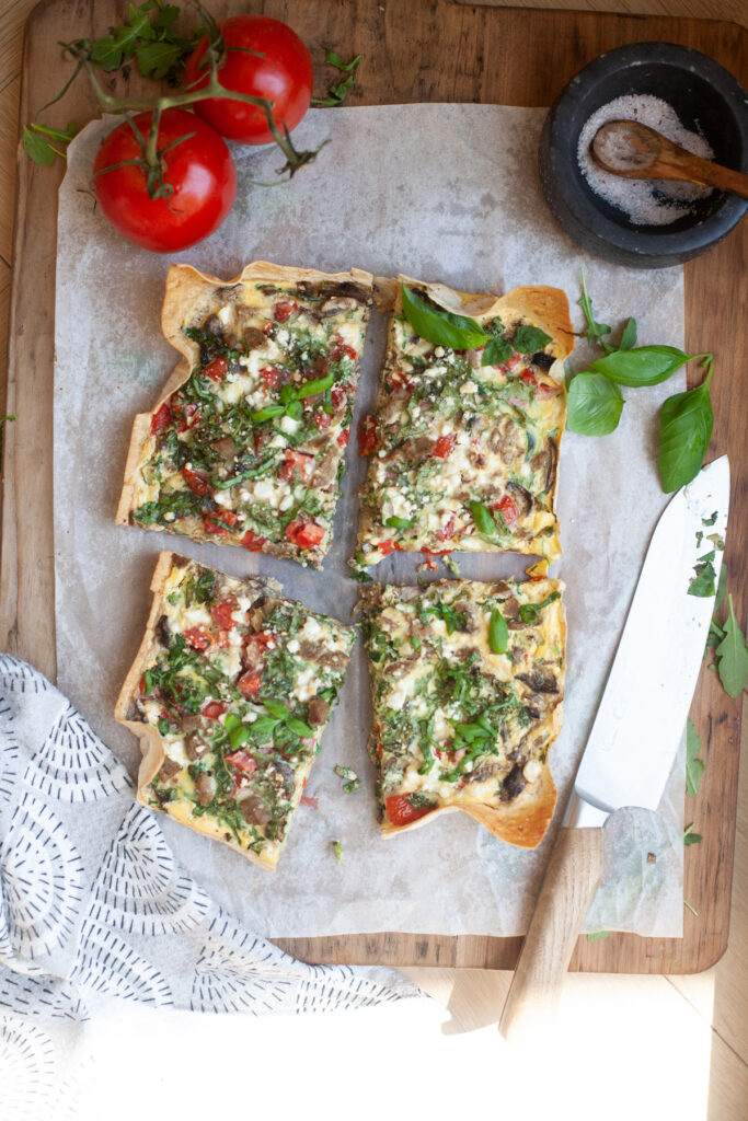 Garden veggie quiche sliced into four squares on parchment paper.