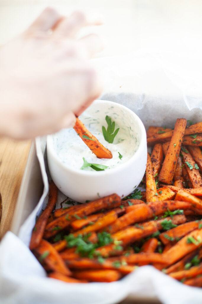 hand dipping into Spicy Carrot Fries with Lemon Cumin Yogurt Sauce | macro friendly sides recipe by www.lillieeatsandtells.com