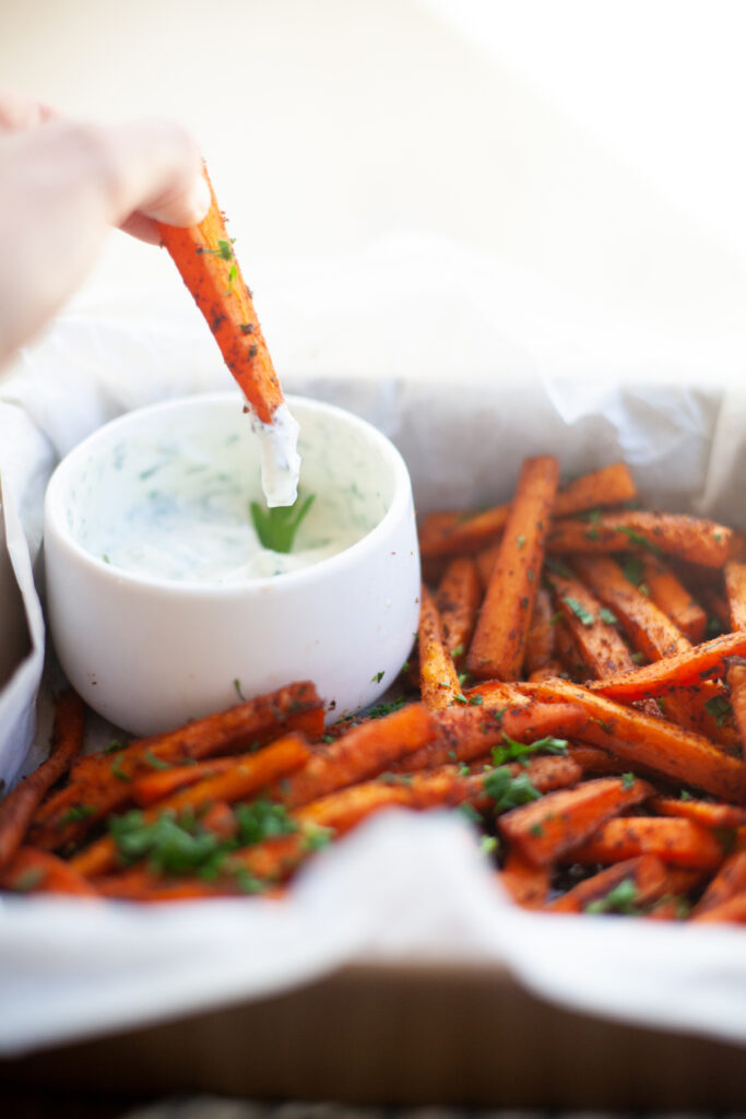 hand dipping into Spicy Carrot Fries with Lemon Cumin Yogurt Sauce | macro friendly sides recipe by www.lillieeatsandtells.com