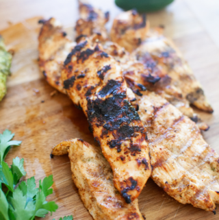 Honey chipotle grilled chicken breast strips with char marks on a wooden cutting board, garnished with fresh parsley and a jalapeño pepper in the background.