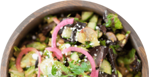 A wooden bowl filled with a fresh salad, including mixed greens, cucumber slices, pickled red onions, fresh cilantro, crumbled cheese, and seeds—a perfect choice for those seeking macro friendly meal prep recipes.