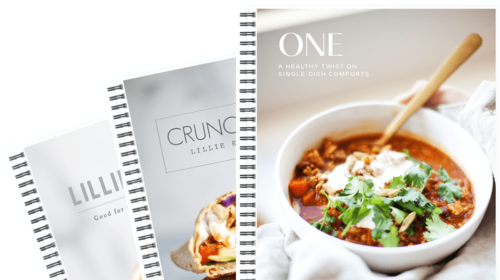 Three spiral-bound cookbooks are fanned out. The front book shows a bowl of chili with sour cream and cilantro, titled ONE: A Healthy Twist on Single-Dish Comforts—perfect for anyone seeking macro friendly dinner recipes. The others partially display wrap sandwiches, suggesting even more delicious macro friendly recipes inside.
