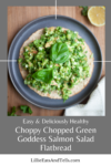 A flatbread topped with a vibrant chopped green goddess salmon salad and fresh basil is displayed on a plate, with a lemon wedge and napkin nearby. Text below describes it as Choppy Chopped Green Goddess Salmon Flatbread.