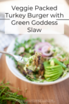 A close-up of a Veggie Packed Turkey Burger with Green Goddess Slaw bowl shows sliced avocado, red onions, crisp green slaw, and a fork holding a juicy piece. Text overlay reads, Veggie Packed Turkey Burger with Green Goddess Slaw.