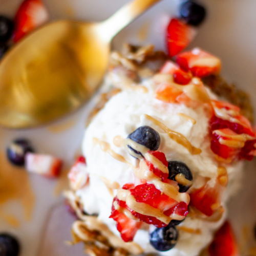 Lemon blueberry zucchini oats in bowl with whipped cream, strawberries, peanut butter and blueberries.