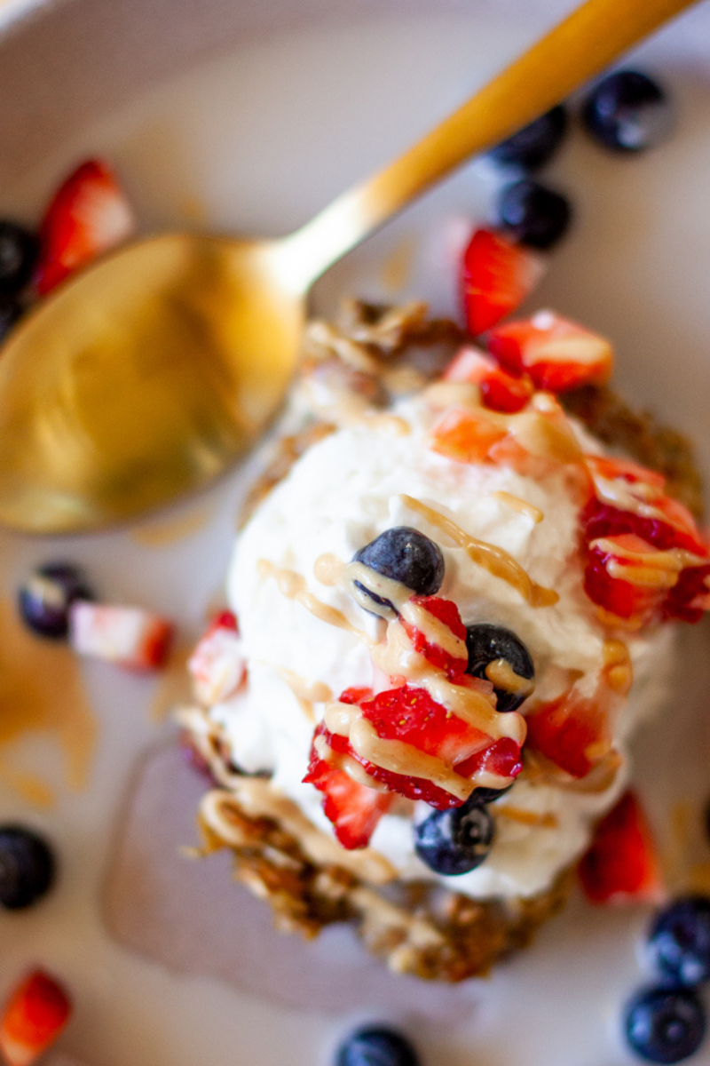 Lemon blueberry zucchini oats in bowl with whipped cream, strawberries, peanut butter and blueberries.